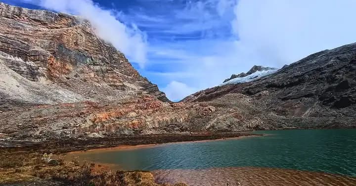 Laguna de aguas verdes enmarcada por montañas rocosas de tonos marrones.