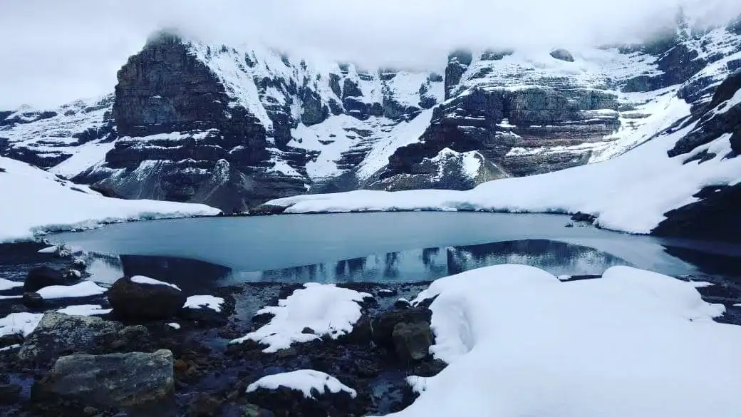 Laguna rodeada de rocas y nieve en alta montaña.