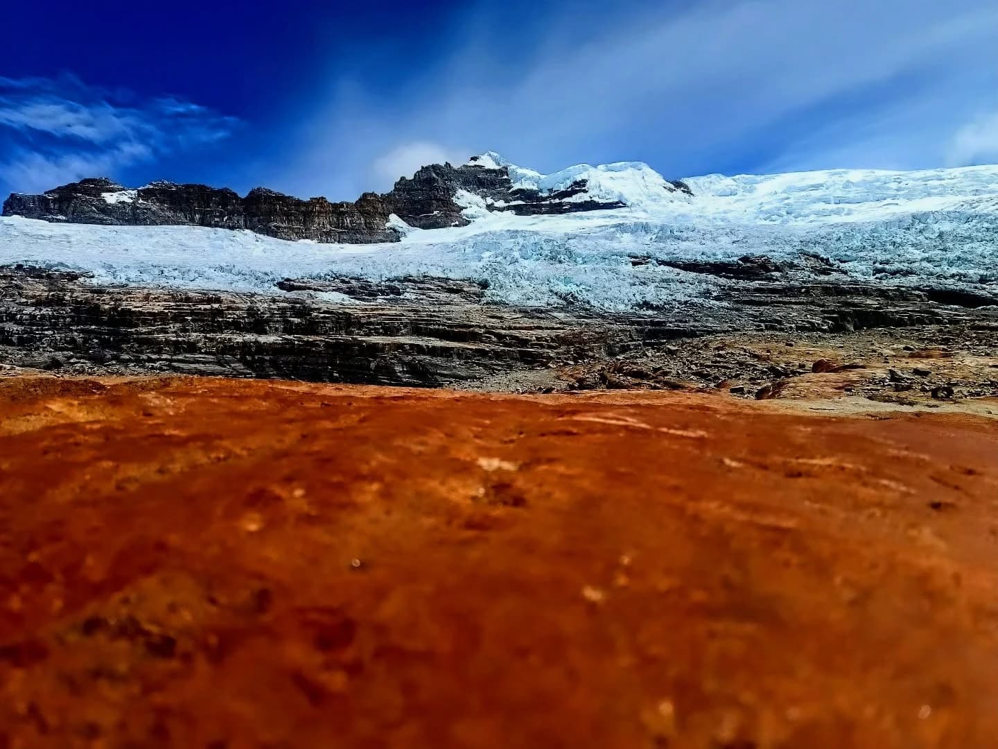 Terreno rojizo en primer plano con un casquete de hielo o glaciar en el fondo.