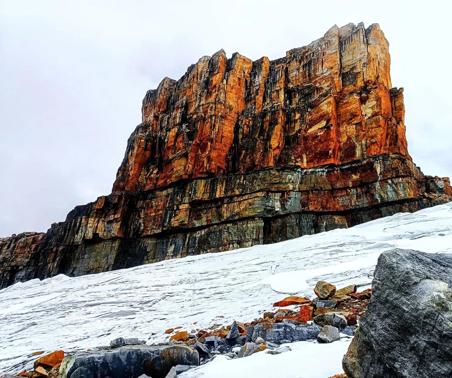 Pared rocosa rojiza tipo meseta con nieve en la base; estratos visibles en la roca.